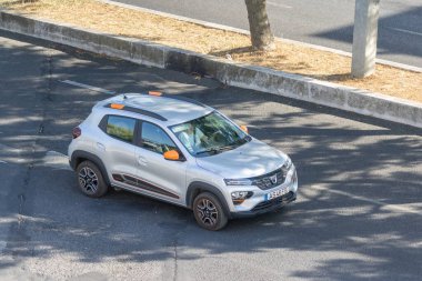 Modern gümüş kaplama elektrikli araba beton kaldırımın yanındaki asfalt yolda gidiyor.