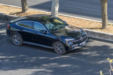 Yol kenarına park etmiş parlak siyah Mercedes Benz GLC Coupe modern tasarımı ve lüks cazibesini sergiliyor.