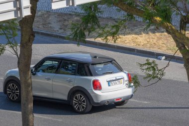 Gümüş rengi mini Cooper, güneşli bir günde şehir yolunda araba sürüyor.