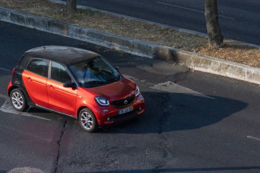 Asfalt yolda ağaçlarla kaplı kırmızı akıllı bir araba sürüyordu.