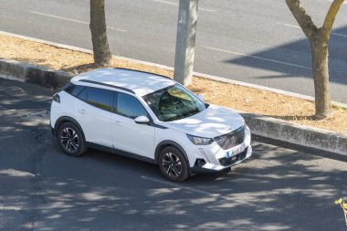 Beyaz peugeot 2008 SUV yol kenarına park edilmiş güneşli bir günün tadını çıkarıyor.
