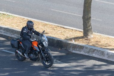 Bisikletli, asfalt yolda, kaldırım ve ağacın yanında 390 macera motosikleti sürüyor.