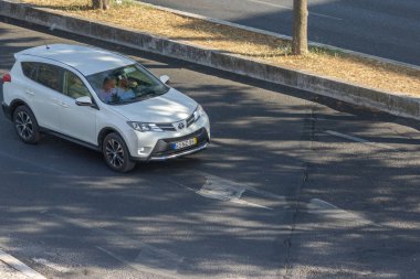 Beyaz toyota rav4 araba şehrin asfalt yolunda gidiyor.