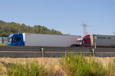 Maersk ve okutman kamyonları güneşli bir günde otobanda mal taşıyorlar.