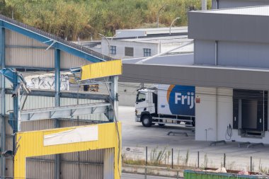 Beyaz Frijj teslimat kamyonu hasarlı cephe ile deponun önüne park edilmiş.