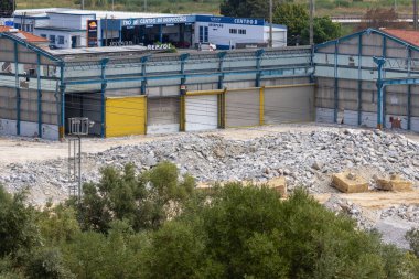 Önünde büyük bir moloz yığını ve yeşil ağaçlarla birlikte bir sanayi binasının söküldüğü yıkım alanı