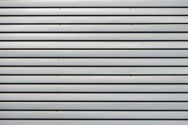Close up of a corrugated metal wall showing a regular pattern of horizontal lines and screws, creating a textured industrial background