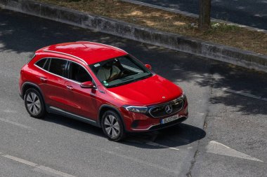 Red mercedes benz eqa electric suv driving on an asphalt road during daylight