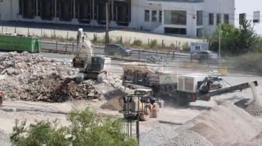 Zaman atlamalı Kazıcı inşaat alanındaki ezilmiş taşları kamyona yüklüyor