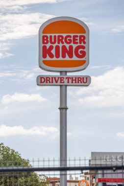 Burger king sign indicating the presence of a drive through service, set against a backdrop of a cloudy sky