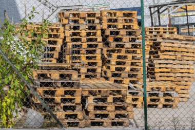 Wooden pallets stacked behind a chain link fence at a construction site, ready for use in logistics and transportation