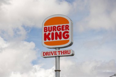 Burger king sign displays its logo and drive thru service availability under a cloudy sky