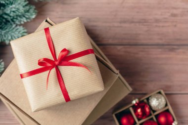 Noel kutlaması için hediye karton kutuları. Dekoratif kırmızı kurdele ve kırmızı cam toplar ahşap arka planda. Noel ve yeni yıl için el yapımı bir hediye. En üstten görüntüle.