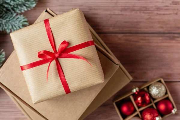 Noel kutlaması için hediye karton kutuları. Dekoratif kırmızı kurdele ve kırmızı cam toplar ahşap arka planda. Noel ve yeni yıl için el yapımı bir hediye. En üstten görüntüle.