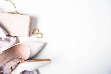 Beige heeled shoes, handbag and earrings are on a white background. Elegant accessories for a wedding or in a restaurant. Copy space.
