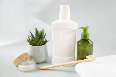 Toothbrush made of natural material, mouthwash and aloe flower with bath accessories of personal hygiene are on a gray background. 