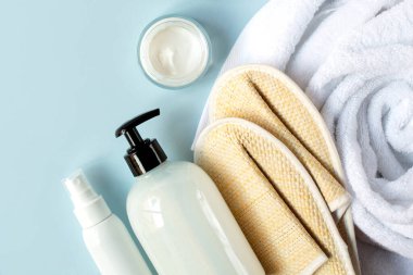 Kozmetik kremler, banyo pipetli terlikler ve beyaz havlu mavi arka planda. Temamız spa ve vücut bakımı..