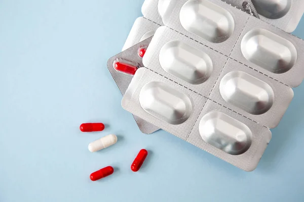 stock image Metallic blister with tablets and pills in red and white are on a blue background.