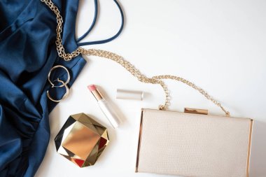 Açık arkaplanda kadınların altın renkli aksesuarları, el çantası ve mavi renkli kokteyl elbisesi bulunuyor. Boşluğu kopyala.