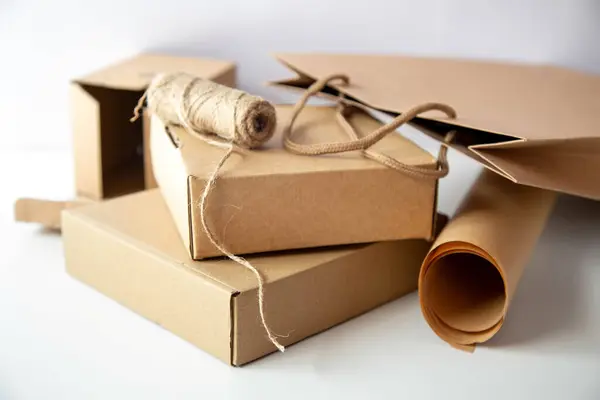 Cardboard boxes of various shapes, paper bag and paper roll and rope are placed on a light background. The theme is natural and recycled product.