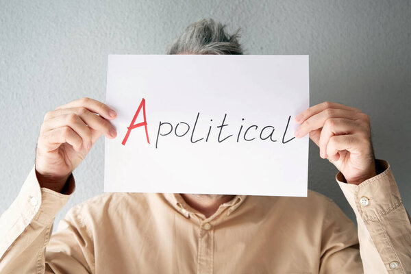 Мужчина в бежевой рубашке держит перед лицом лист бумаги с надписью - аполитичный.