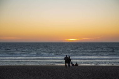 Günbatımı gökyüzü ve okyanusun arka planında insanların siluetleri. Akşam deniz manzarası, gün batımı renginde gökyüzü..