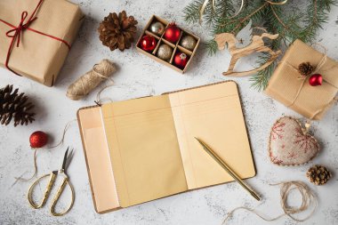 Masada güzel Noel süsleri ve paketlenmiş hediyelerle çevrili açık bir defter var. Yeni yıl için planlar ve hazırlıklar. Boşluğu kopyala.