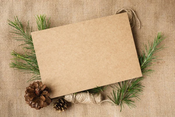 Resmin ortasında bir mukavva yaprak, bir tuval arka planında bir Noel süsü ve ladin dalları ve koniler ile çevrili. Retro tarzı. Boşluğu kopyala.