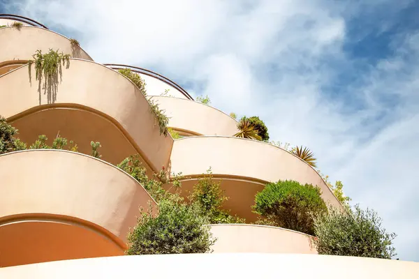 View of residential buildings with flowering rounded terraces against a blue sky with white clouds. European architecture.