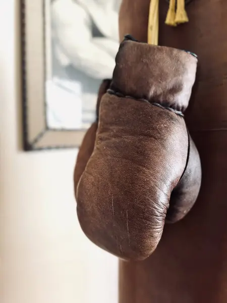 Boxing leather gloves in brown hanging on a punching bag are a close-up. Retro style. Vertical image.