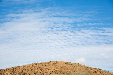 Tepenin üstündeki mavi gökyüzünde bulutlu dalgalar. Arka plan mavi bir gökyüzü ve bir tepe..