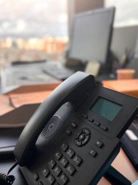 Telefon bir ofis masasında, arka planda bir bilgisayar ve şehir manzarası bulanık bir pencere var..