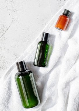 Üzerinde spa ürünleri olan üç şişe, gri arka planda beyaz bir banyo havlusu var. Üst Manzara. Dikey resim.
