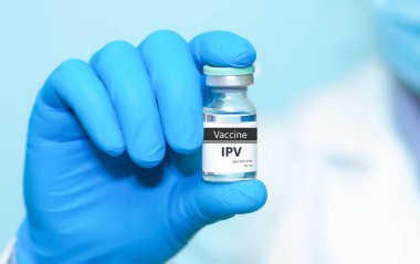 IPV (pasif poliovirüs) aşı şişesini mavi arka planda tutan koruyucu tıbbi eldiven giyen doktor, sağlık, modern tıp, hastalık önleme ve aşılama bilincini sembolize ediyor