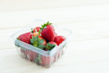 Plastik kabın içinde taze kırmızı çilekler ve ahşap arka plan.