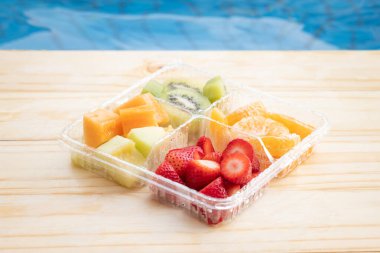 Plastik kabın içinde sağlıklı meyvelerin karışımı; çilek, kivi, portakal, kavun