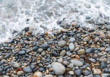 Farklı boyutlarda yuvarlak taşlar ve deniz suyuyla yıkanmış kumsalda gri tonlarda..