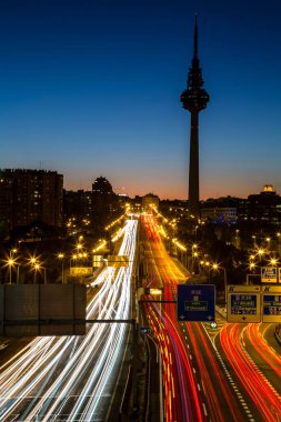 Arkaplanda Torrespania iletişim kulesi ve trafik ışıkları çizgileri olan Madrid siluetinin günbatımı görüntüsü.