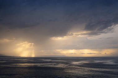 Ufuktaki bulutlar arasında gün batımı manzarası. Bulutlarda ve denizde altın yansımalar.