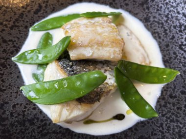 Beyaz bir tabakta sunulan bezelyeli pişmiş balık tabağının üst görüntüsü..