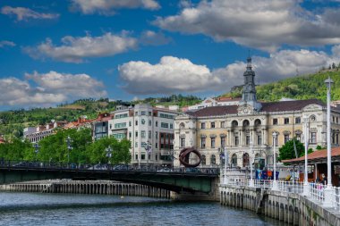 Önünde Nervion nehri olan Bilbao şehrinin manzarası ve arkasında da bir yaz gününde mavi gökyüzü ve beyaz bulutlar olan belediye binası..