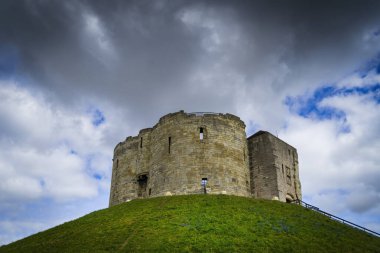 Antik Clifford kulesi alacakaranlıkta yeşil bir tepede ve mavi gökyüzü arka planda kara bulutlarla. İngiltere 'deki York City..