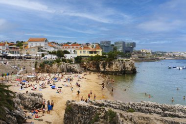 Portekiz 'in Cascais kentindeki bir deniz kıyısında canlı bir yaz sahnesi. İnsanlar rahatlar ve kumsalda güneşlenirler..