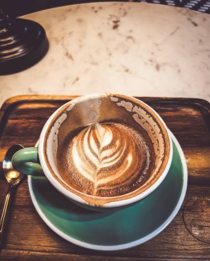 Sıcak bir kapuçino, sıcak bir atmosferde masanın üzerine konmuş içme bardağındaki kahve..