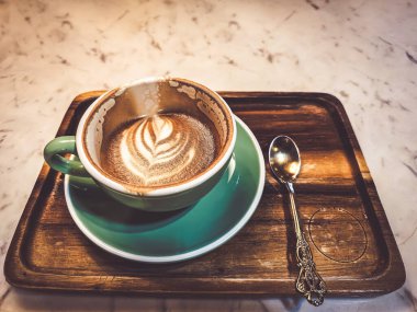 Sıcak bir kapuçino, sıcak bir atmosferde masanın üzerine konmuş içme bardağındaki kahve..