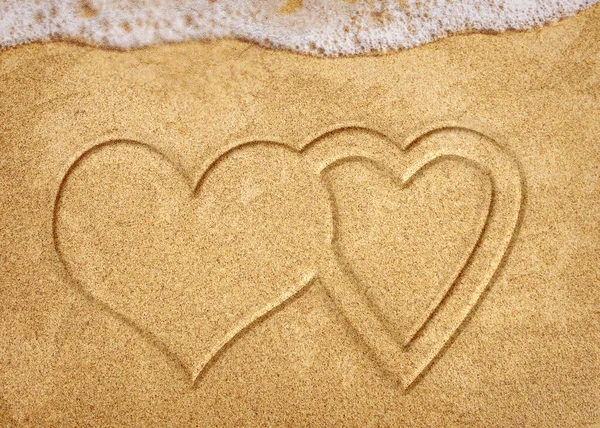 Two hearts handwritten on sand of tropical beach, background