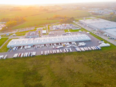 Gün batımında yükleme / boşaltma malları için rampalarda bekleyen depo, merkez ve kargo karavanıyla lojistik parkının hava görüntüsü.