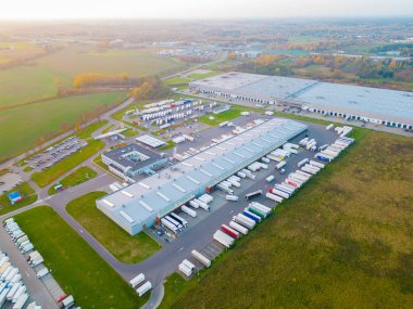 Gün batımında yükleme / boşaltma malları için rampalarda bekleyen depo, merkez ve kargo karavanıyla lojistik parkının hava görüntüsü.