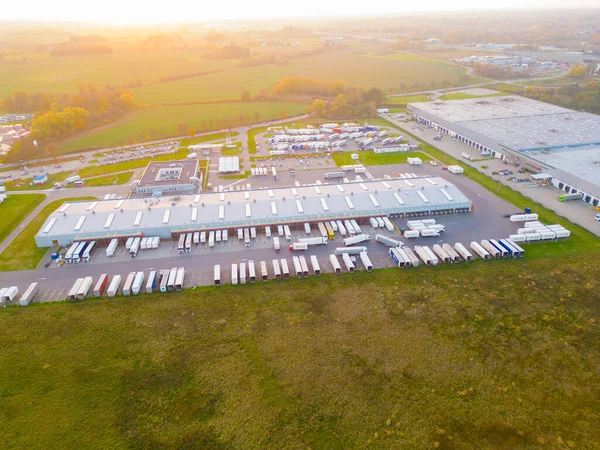 Gün batımında yükleme / boşaltma malları için rampalarda bekleyen depo, merkez ve kargo karavanıyla lojistik parkının hava görüntüsü.