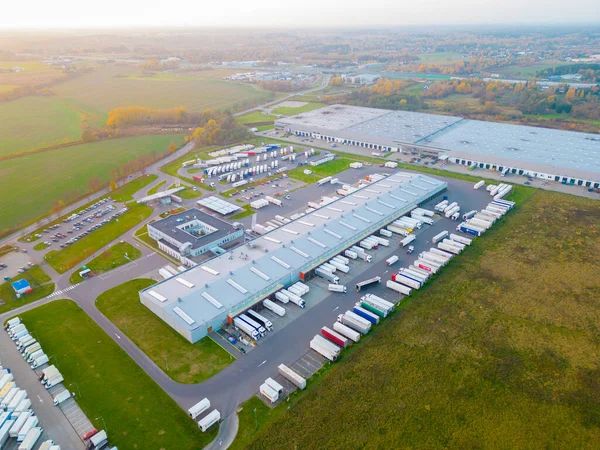 Gün batımında yükleme / boşaltma malları için rampalarda bekleyen depo, merkez ve kargo karavanıyla lojistik parkının hava görüntüsü.